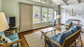 Een ruime woonkamer met grote ramen, rieten meubels en een televisietoestel.