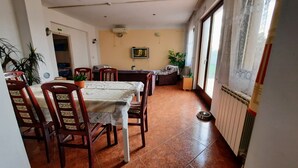 Un coin repas avec une table dressée pour quatre personnes, entourée de chaises, un téléviseur fixé au mur et un radiateur le long du mur.