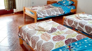 Une chambre avec deux lits en bois, dotés de draps à motifs, un radiateur, un tableau représentant une plage et une fenêtre avec des rideaux.