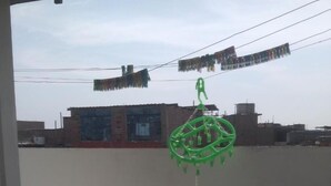 A balcony with a green hanging decoration, tiled floor, and a view of buildings in the background. - Beautiful, central and economical apartment (Rímac)