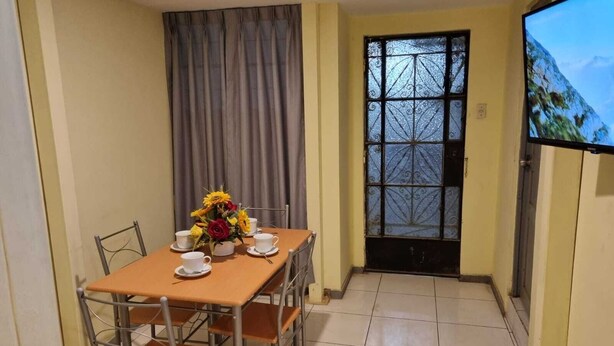 A dining area with a table set for four, chairs, a flower centerpiece, and a TV on the wall. - Beautiful, central and economical apartment (Rímac)