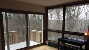A room with a wooden floor, a desk, and a view of a deck and trees through large windows. - Sweet and spacious mountain view home w/fireplace! (Gardiner)