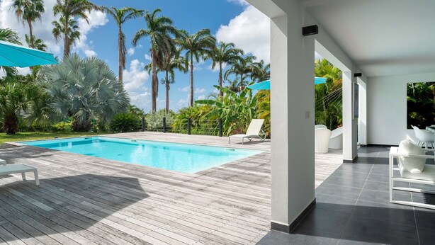 A modern pool area with a wooden deck, white lounge chairs, and a view of palm trees.