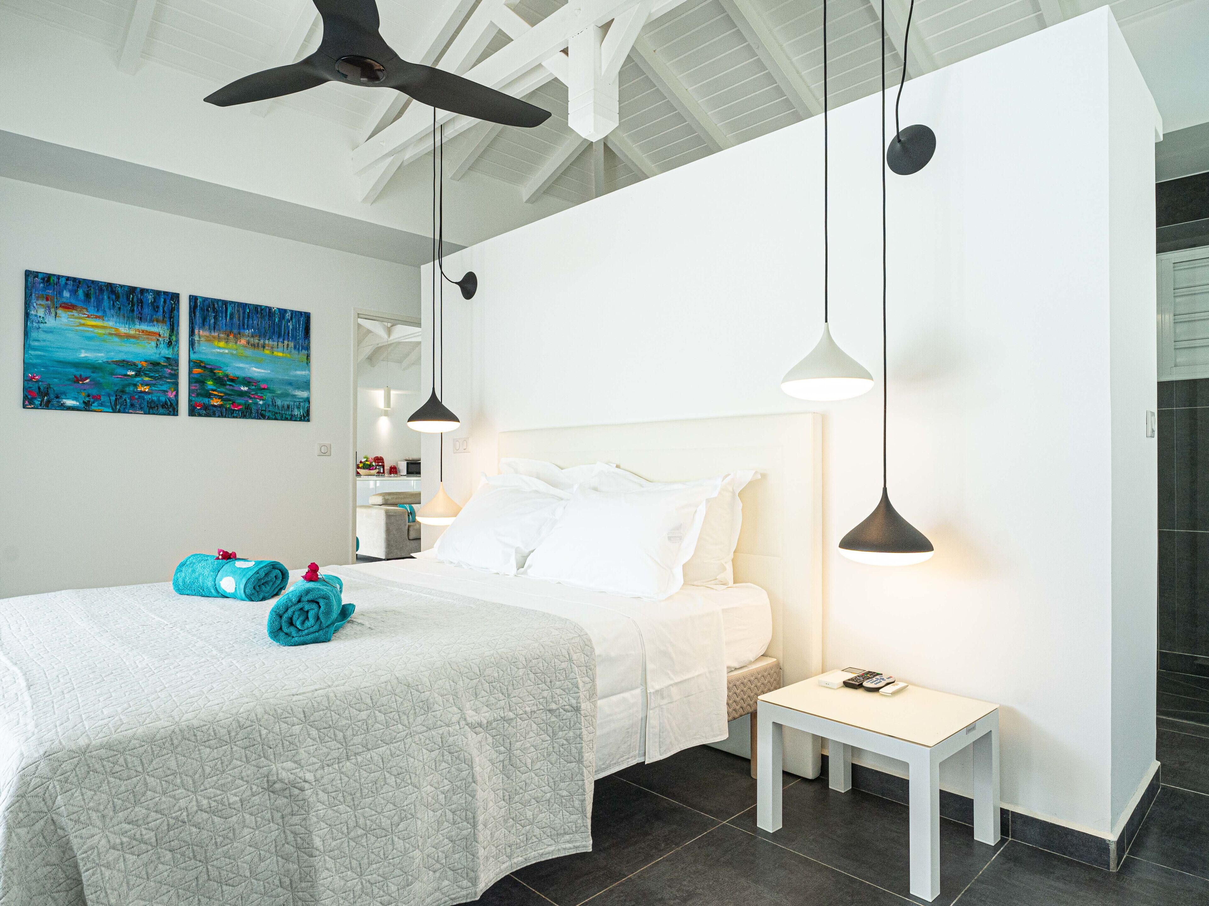 A modern bedroom with a large bed, a small bedside table, and a ceiling fan.
