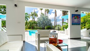 A modern living room with a pool view, white furniture, and a glass table with a drink.