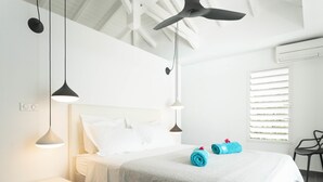 A modern bedroom with a bed, two pendant lights, a ceiling fan, a bedside table, and a window with blinds.