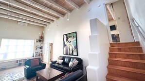 A spacious living room with a high ceiling, a staircase, and a large window. - Charming Santa Fe Adobe Home 2 BR w/Elevated Views (Santa Fe)