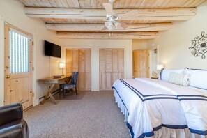 A bedroom with a bed, a desk, a chair, a ceiling fan, and wooden doors.