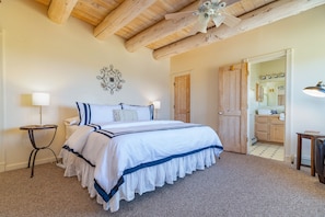 Quarto com uma cama grande, um ventilador de teto, uma porta de madeira e um banheiro visível através de uma porta aberta.