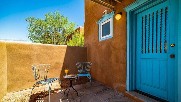 A patio with two metal chairs and a small table, a blue door with a decorative pattern, and a small window with a light fixture. - Charming Santa Fe Adobe Home 2 BR w/Elevated Views (Santa Fe)
