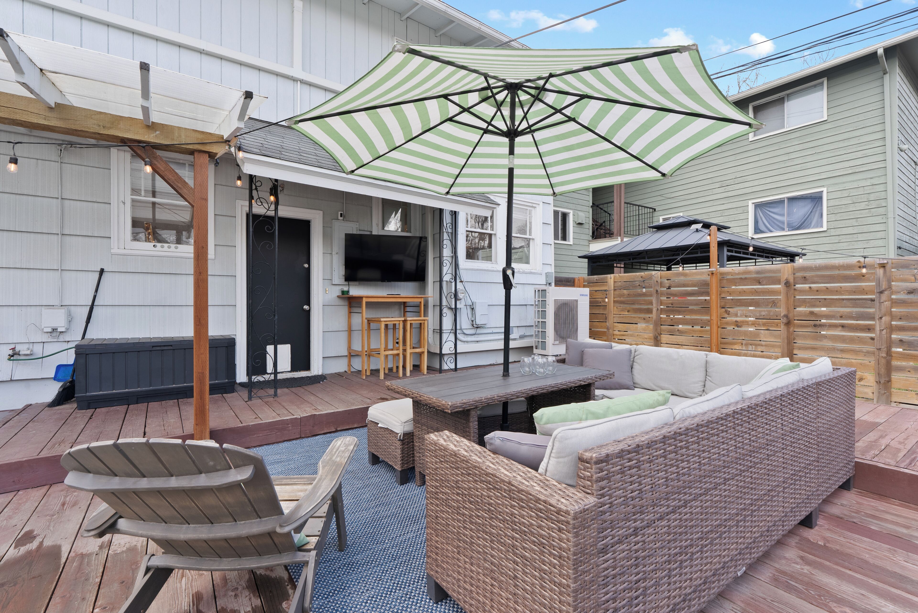 Une terrasse dotée de meubles en osier, d’un parasol à rayures et d’une plateforme en bois.