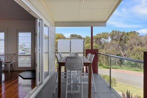Un balcon avec une table et des chaises, une porte-fenêtre coulissante et une vue sur des arbres et une route.
