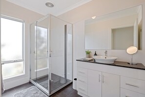Une salle de bain moderne avec une douche à l’italienne en verre, un lavabo blanc et un grand miroir.