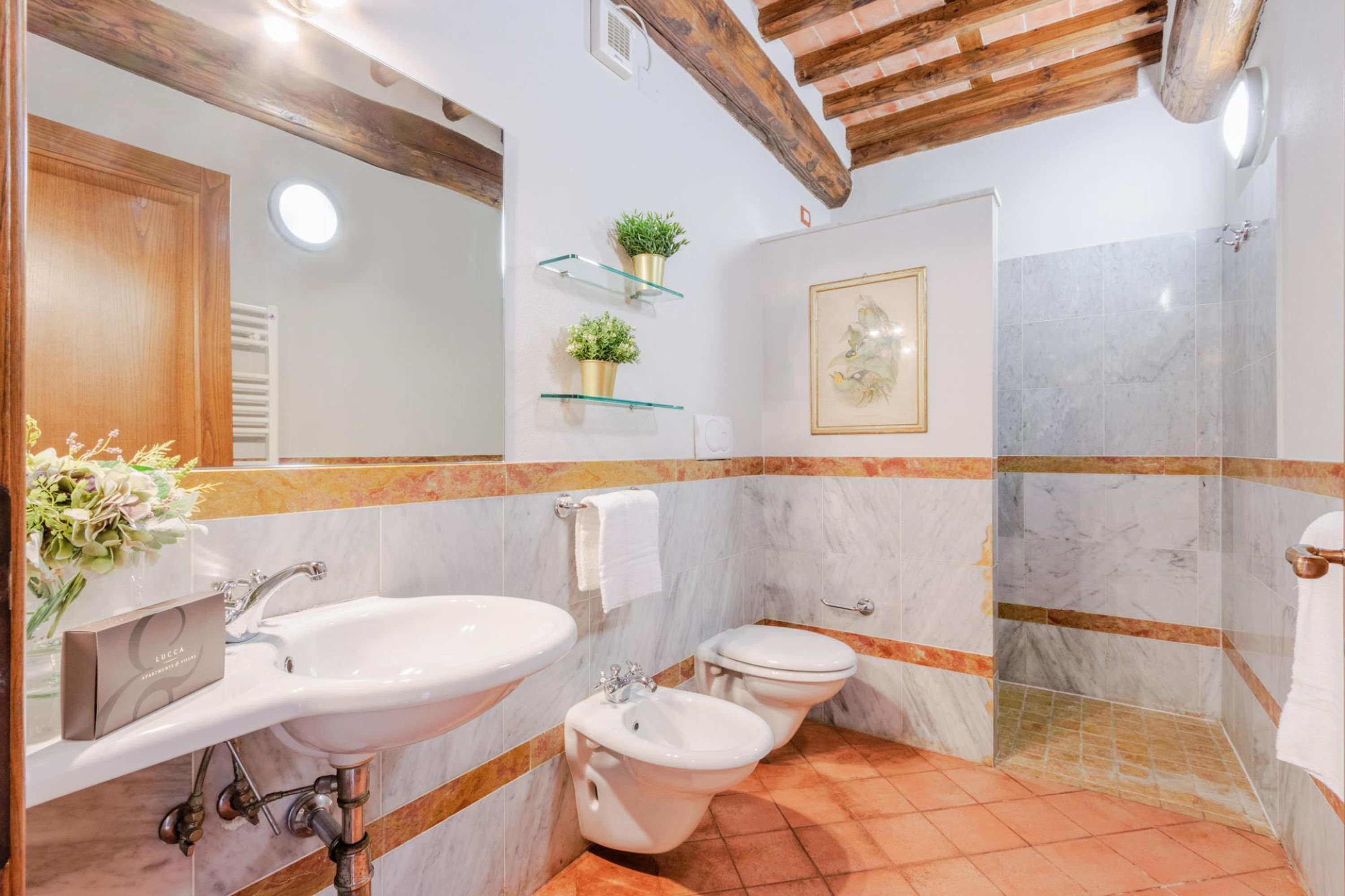 Ein Badezimmer mit Waschbecken, Bidet und Dusche. Pflanzen stehen auf Regalen und ein gerahmtes Bild hängt an der Wand.