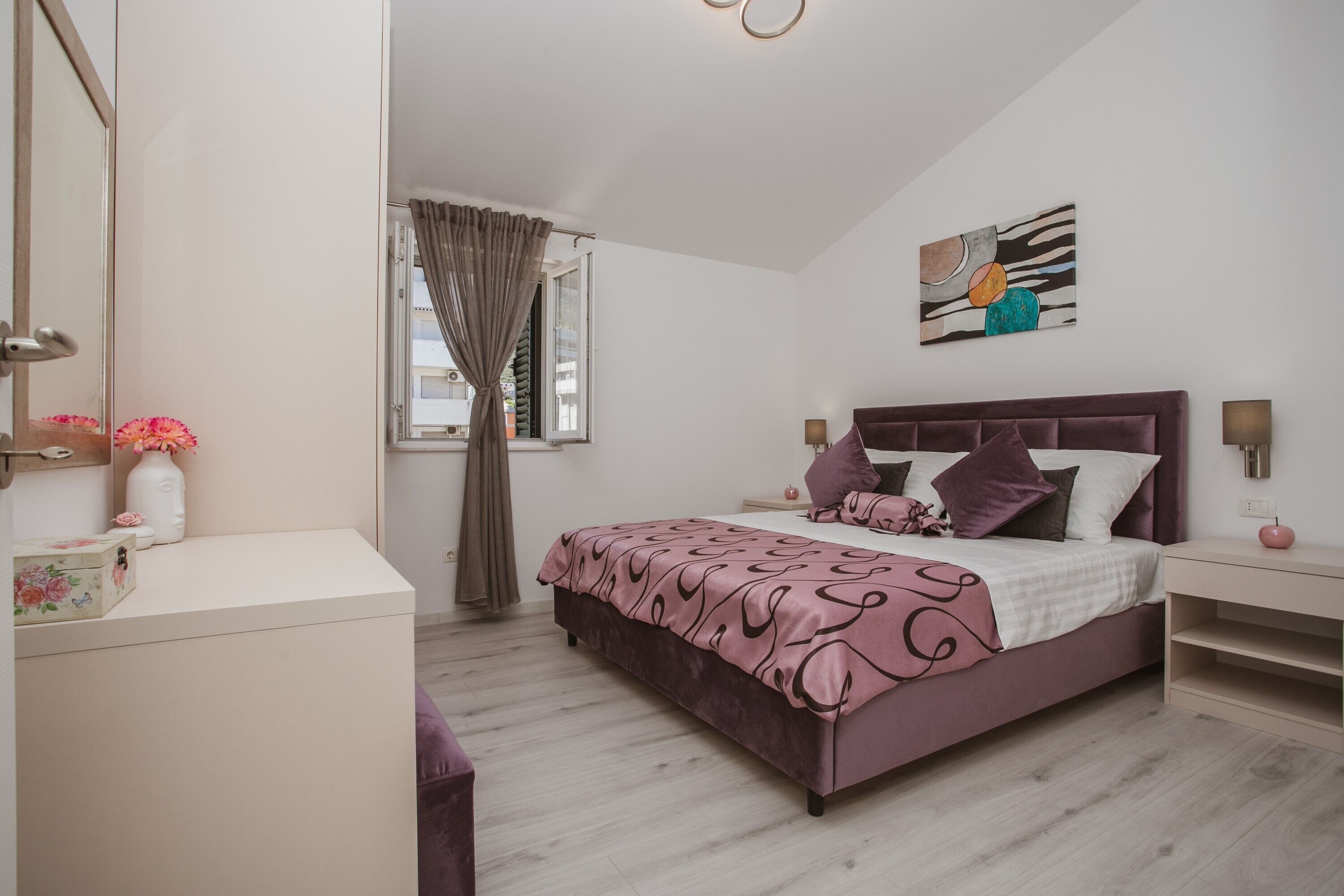 A bedroom with a bed, bedside tables, a dresser, a window with curtains, and a wall-mounted artwork.