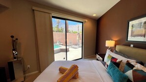 Ein Hotelzimmer mit Bett, Schreibtisch, Lampe und Blick auf einen Außenpool und Palmen.