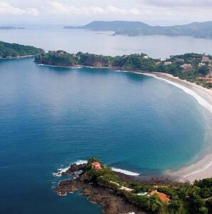 Vista aérea de una zona costera con playa, afloramientos rocosos y abundante vegetación.