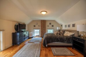 A bedroom with a bed, dresser, and a television on a dresser. There are two windows and a brick wall. - Cayuga Street Retreat (Lewiston)