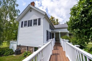 A two-story house with a covered porch and a wooden deck. - Cayuga Street Retreat (Lewiston)