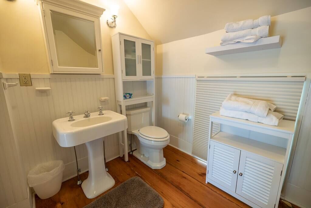 Ein Badezimmer mit einem Standwaschbecken, einer Toilette, einem Spiegel und einem Handtuchregal.
