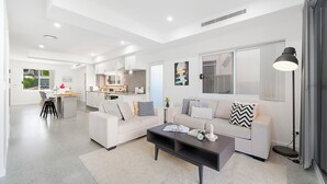 A modern living room with a sofa, coffee table, and a dining area with chairs and a kitchen in the background.