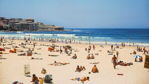A crowded beach with people sunbathing and swimming.