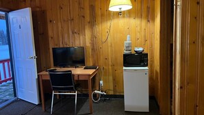 A compact room with wooden walls, a desk with a computer, a television, a refrigerator, and a bed. - Glacier View Inn (Haines Junction)