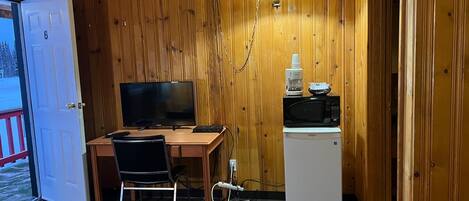 Een compacte kamer met houten wanden, een bureau met computer, een televisie, een koelkast en een bed.