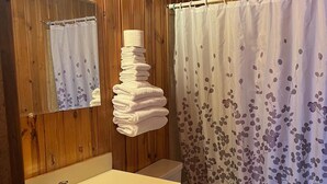 A bathroom with wooden paneling, a sink, a toilet, and a shower curtain with a floral pattern. - Glacier View Inn (Haines Junction)