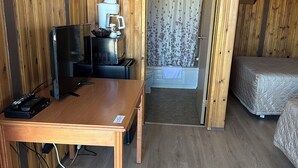 A wooden room with a bed, a table with a TV, a coffee machine, and a shower area.
