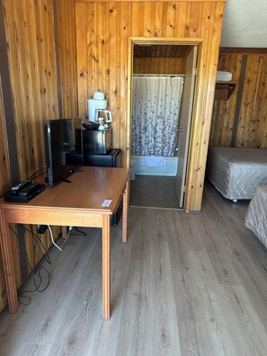 A wooden room with a bed, a table with a TV, a coffee machine, and a shower area. - Glacier View Inn (Haines Junction)