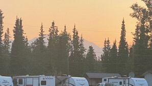 A row of RVs and a car parked in a grassy area with a mountain in the background. - Glacier View Inn (Haines Junction)
