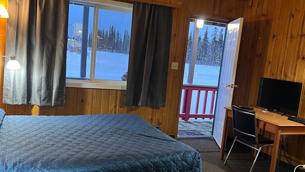 A room with a bed, a desk, a TV, and a window with curtains. - Glacier View Inn (Haines Junction)