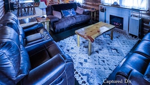 Un intérieur chaleureux de chalet en bois, avec une cheminée, des canapés en cuir, un téléviseur et un coin repas.