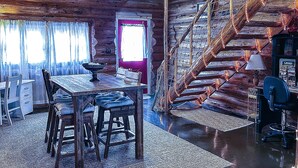 L’intérieur d’un chalet rustique comprend une table à manger en bois, des chaises, un escalier et un petit espace aménagé en bureau.
