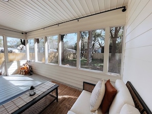 A covered patio with a table and chairs, a sofa with cushions, and large windows offering a view of the backyard.
