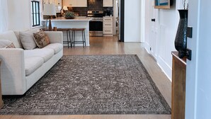Une cuisine moderne avec un îlot central, un coin repas agrémenté d’un lustre, et un salon avec un canapé et un tapis.