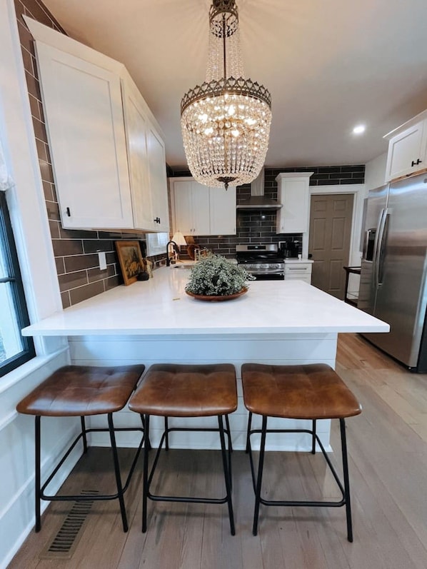 A kitchen with a central island, bar stools, a chandelier, and modern appliances.