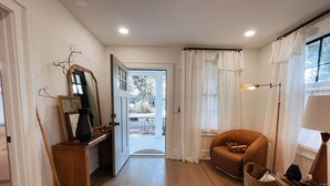 Un couloir doté d’un plancher en bois, d’un fauteuil marron, d’une lampe et d’une porte donnant sur l’extérieur.