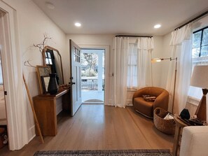 A room with a wooden floor, a brown armchair, a lamp, and a door leading to an outdoor area.
