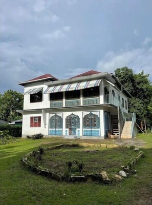 Stunning two-story building with a central entrance and decorative grills, surrounded by a beautifully manicured lawn and garden.
