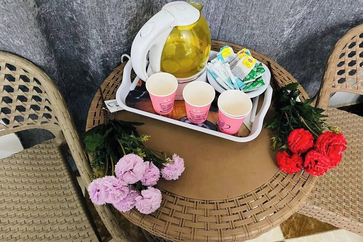 Une table ronde avec un set de table en fibres tressées, un plateau avec des tasses et une théière, et des fleurs.