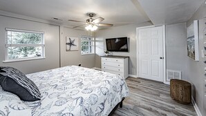 Un dormitorio con cama, ventilador de techo, televisor y una puerta.