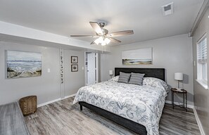 Quarto com cama, ventilador de teto, obras de arte e janela.