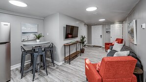 Una sala de estar moderna con un sofá rojo, un televisor montado en la pared y una zona de comedor con mesa y sillas.