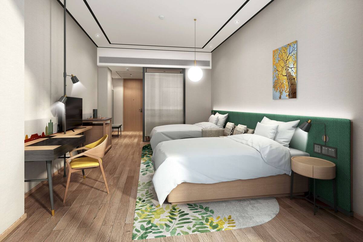 Quarto de hotel moderno com cama, mesas de cabeceira, escrivaninha com cadeira, espelho e um quadro na parede.
