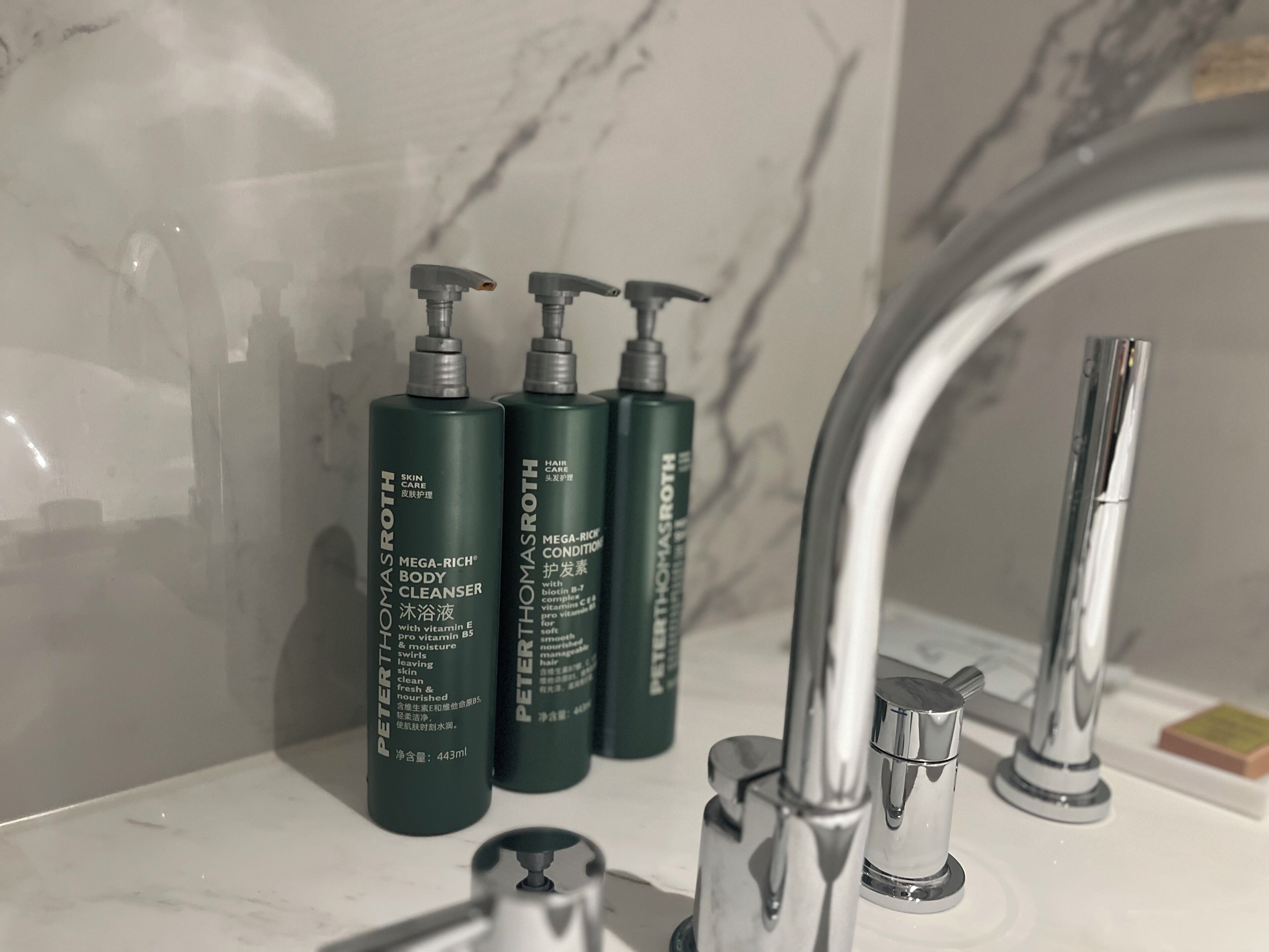 Une salle de bain avec un lavabo en marbre, un robinet moderne et trois flacons de produits de soins pour la peau de la marque « Peter Thomas Roth ».