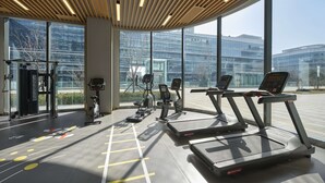 A modern gym with treadmills, exercise bikes, and weight machines. Large windows offer views of a cityscape.