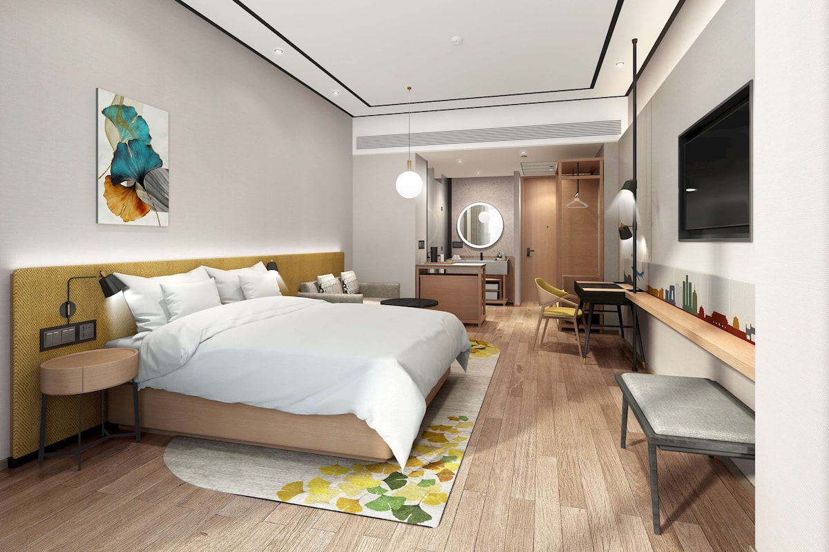 Quarto de hotel moderno com uma cama grande, mesa de cabeceira e uma escrivaninha com cadeira.
