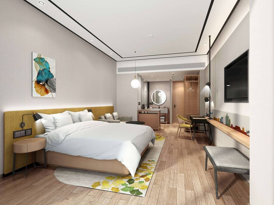 A modern hotel room with a large bed, bedside table, and a desk with a chair.